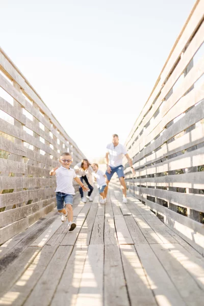 Famille joyeuse courant sur un ponton en bois, enfant devant, parents et fratrie suivant en riant